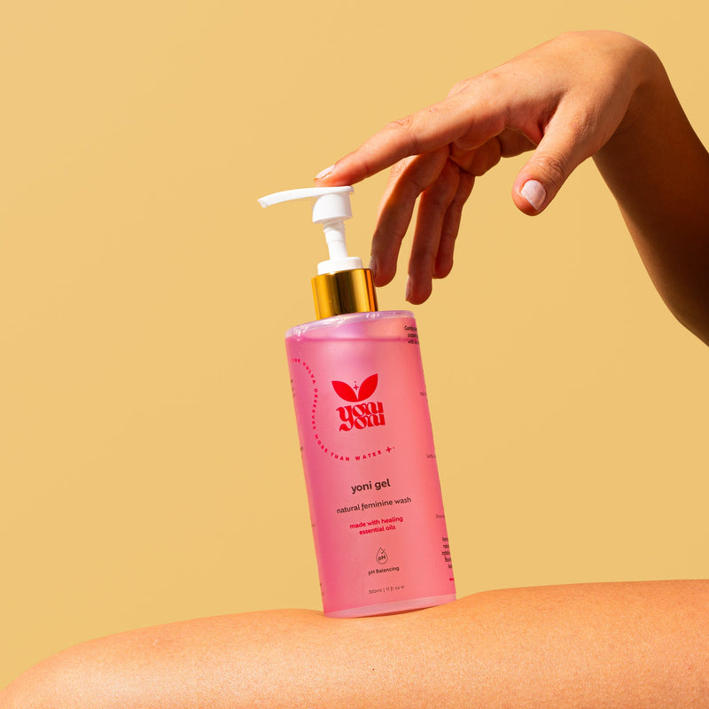 Hand pressing the pump of a Yoni Gel bottle resting on a leg